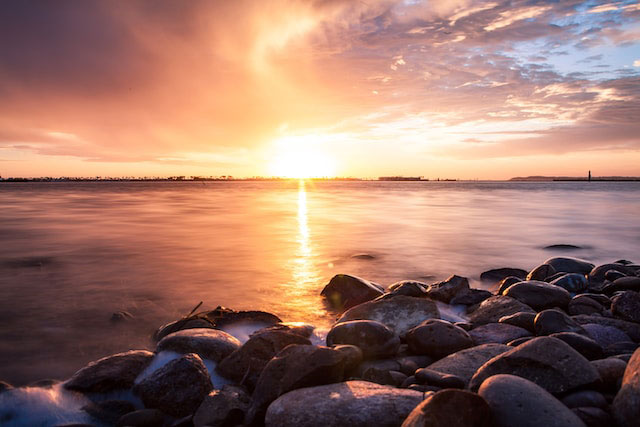 Sunset over a body of water in Chula Vista with rocks in the foreground