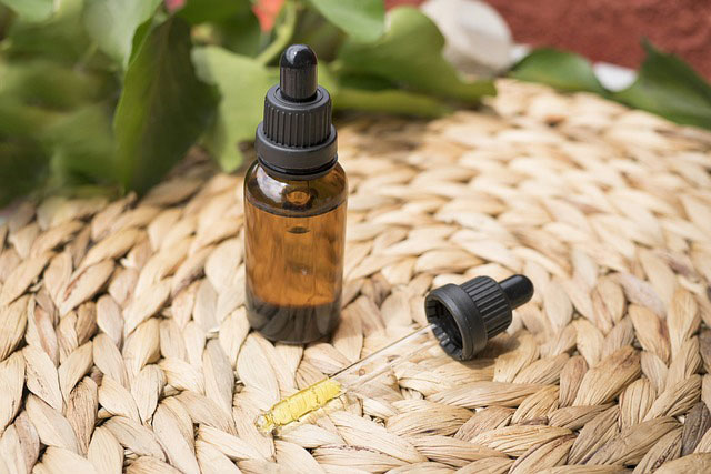 Brown glass bottle and dropper beside it with CBD oil on top of a woven matt