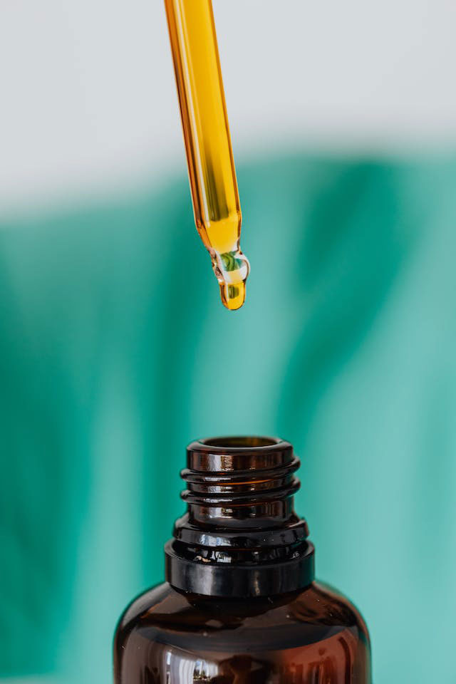 Close-up of a dropper filled with CBD oil and the top part of a brown glass bottle against a white and teal background