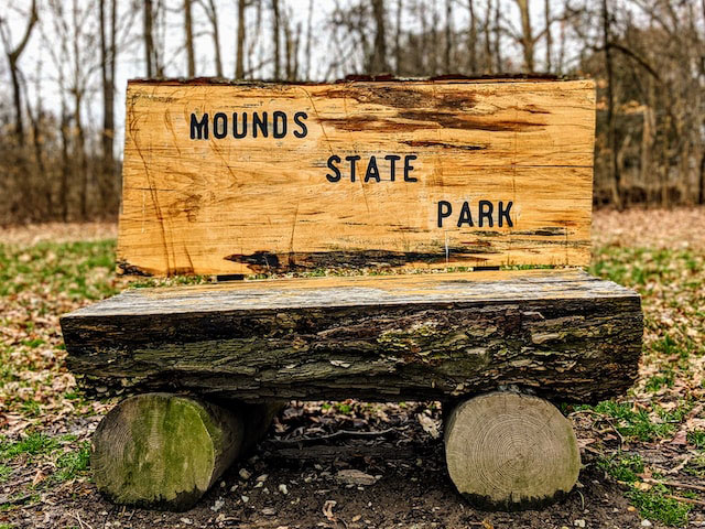 Log bench on a forest trail in Anderson, Indiana that reads "Mounds State Park"