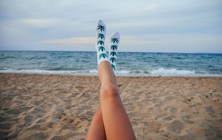 Woman in Cannabis-Leaf-Covered Socks Relaxing on Beach