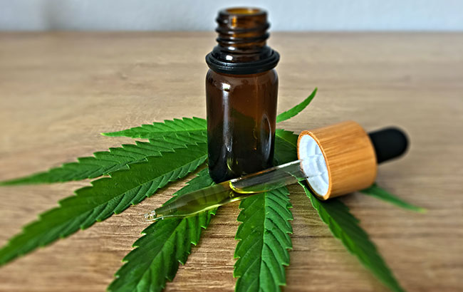 A brown glass bottle and dropper with CBD oil sitting on a cannabis leaf