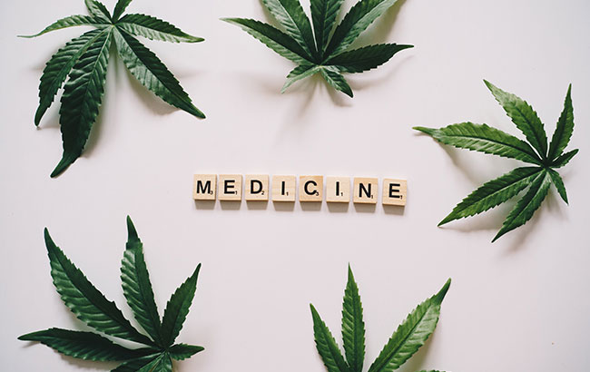 Five cannabis leaves surrounding wooden tiles that spell out "MEDICINE"
