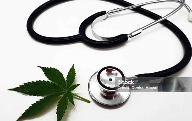 A stethoscope next to a marijuana leaf on a white table 