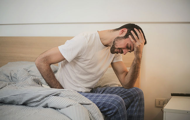 A man slouched on his bed suffering from a headache