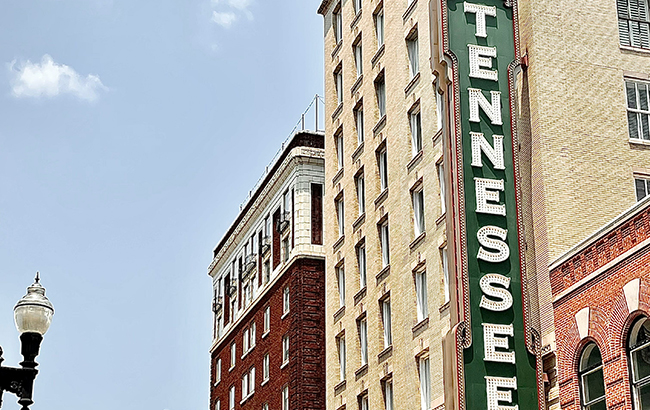 A picture of downtown Tennessee with old brick buildings and an iconic Tennessee sign. The buildings are adorned with American flags.