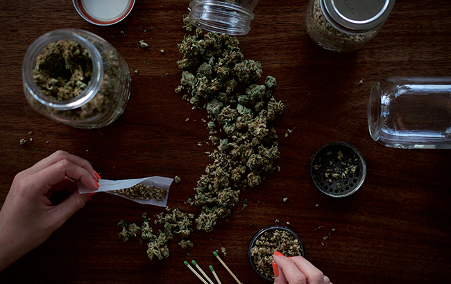 A person rolling marijuana on a table with buds on the table and in jars