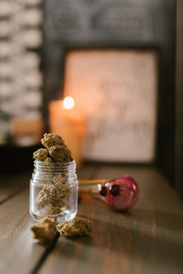 dried cannabis and glass pipe on wooden tabletop