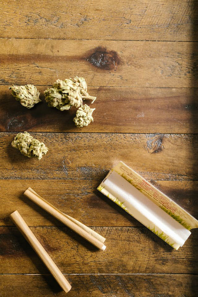 dried cannabis and rolling papers on wooden table