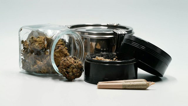 Clear glass container with marijuana buds inside next to cannabis grinder and airtight storage  container
